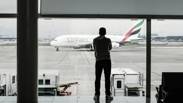 Mężczyzna w bluzie patrzy na samolot Emirates. Czeka na swój bagaż podręczny.