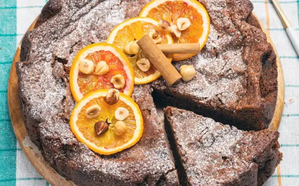 Torta di pane ricetta della nonna, cosparsa di zucchero a velo, decorata con fette d'arancia, nocciole e cannella.