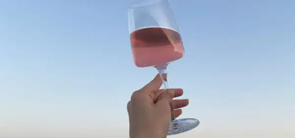 Różowe letnie wino w kieliszku, unoszone na tle błękitnego nieba. Idealny moment na orzeźwienie.