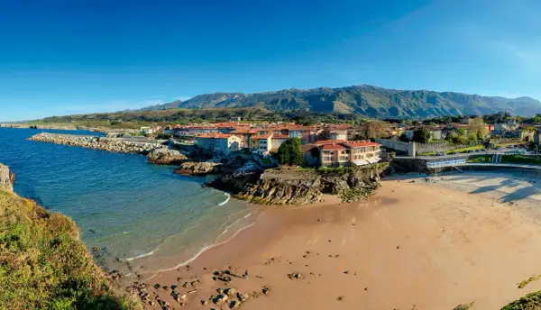 Costa asturiana con playa, pueblo costero y montañas. Descubre qué ver en Nueva de Llanes, un paraíso natural.