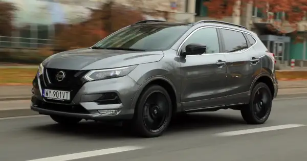 Szary Nissan Qashqai 2019 z czarnymi felgami pędzi ulicą, otoczony jesienną scenerią.
