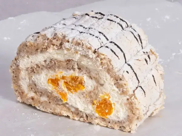 En bit Budapest bakelse med vispgrädde och aprikoser, pudrad med florsocker och dekorerad med choklad.