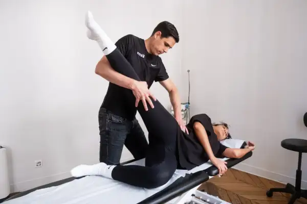 Un kinésithérapeute guide un exercice kiné hanche, soulevant la jambe d'une patiente allongée sur une table de massage.