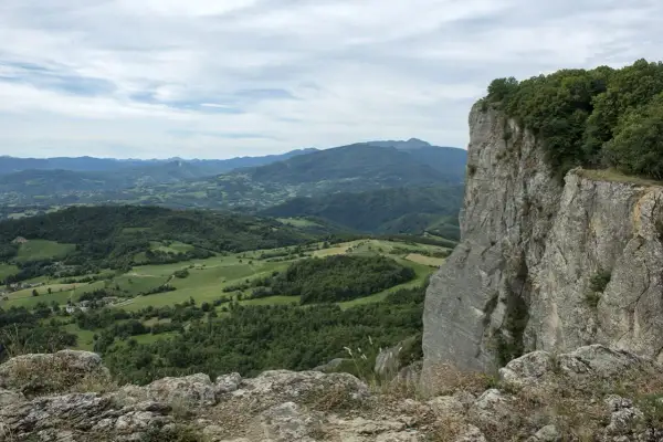Vista panoramica dalla cima della Pietra di Bismantova, con colline verdi e montagne all'orizzonte sotto un cielo nuvoloso.