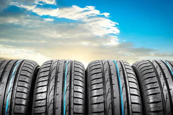 Quatre pneus de voiture, parfaits pour l'été ou toutes saisons, alignés sous un ciel bleu éclatant avec des nuages blancs.