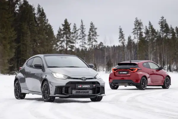 Dwa sportowe toyoty hatchback GR Yaris na śniegu, jeden szary z przodu, drugi czerwony z tyłu, na tle zimowego lasu.