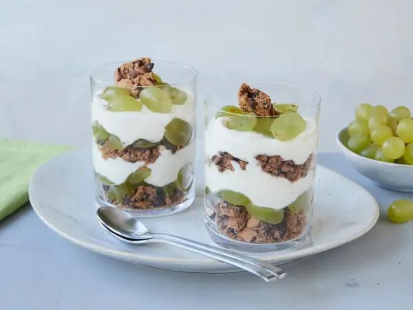 Zwei Gläser mit einem leckeren Trauben-Cookie-Dessert, geschichtet mit Joghurt und Keksbröseln.