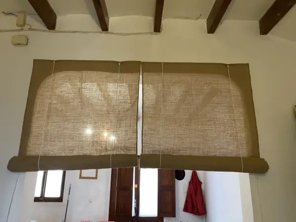 Dos estores enrollables caseros de tela rústica cubren una ventana y una puerta.