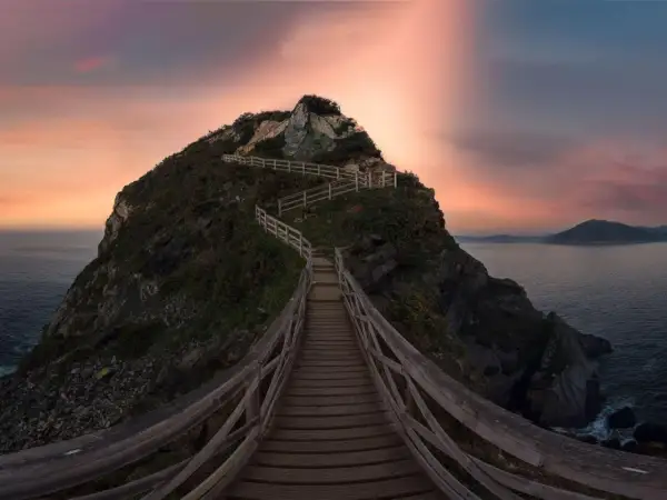 Pasarela de madera serpentea hacia la cima de un acantilado en Galicia, con el mar y un cielo crepuscular de ensueño. Unos de los miradores más espectaculares.