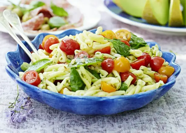 En härlig pastasallad vegetarisk med körsbärstomater, basilika och pinjenötter i en blå skål.