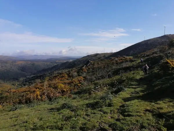 Senderismo en el monte Seixo, con molinos de viento en la cima y un valle verde al fondo.