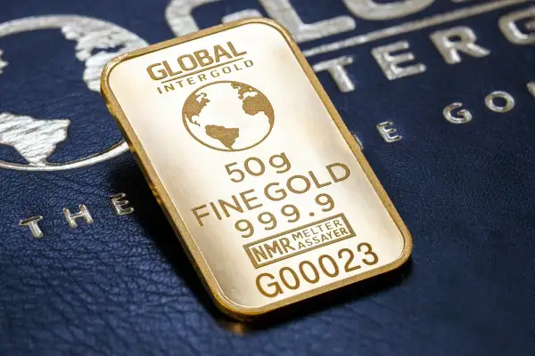 Sztabka złota 50g, czyli ok. 1.6 uncji, z napisem "FINE GOLD 999.9". Na tle ciemnej skóry z wytłoczonym globusem.