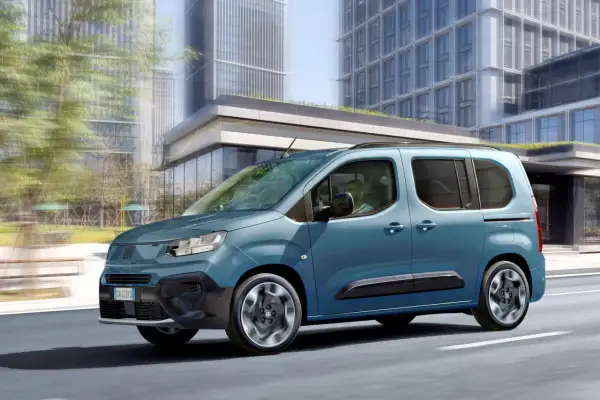 Un Fiat Doblò 9 posti blu metallizzato sfreccia in città, con grattacieli moderni sullo sfondo.