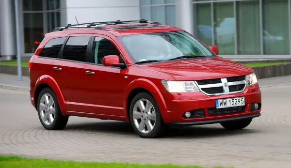 Czerwony Dodge Journey 3.6 z relingami dachowymi jedzie po brukowanej drodze.