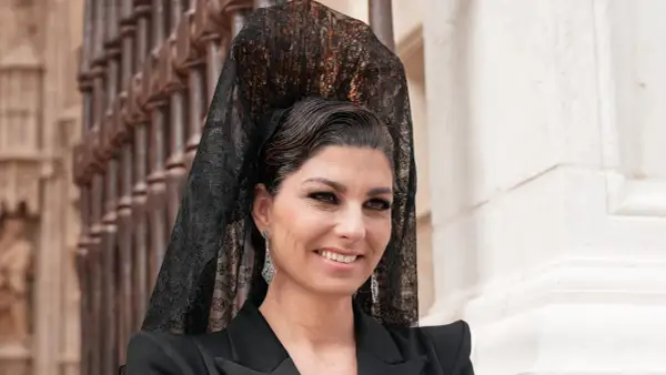 Mujer con peinado boda gitana, velo de encaje negro y pendientes largos. Sonríe con elegancia.
