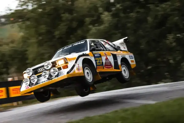 Klasyczny Audi Sport Quattro w akcji, unoszący się nad zakrętem. Ikona rajdów.