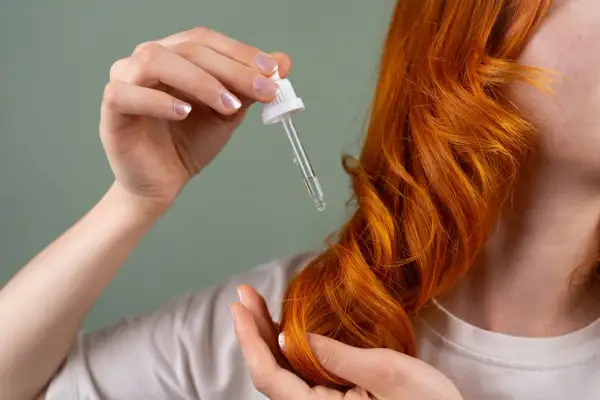 Dłoń z pipetką z olejkiem aplikuje pielęgnację na rude włosy. Dowiedz się, jak często olejować włosy dla najlepszych efektów.