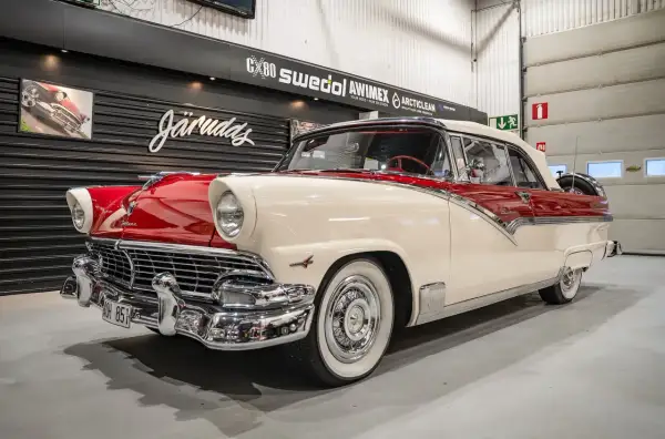 En skinande röd och vit Ford 56 cabriolet står i ett garage.