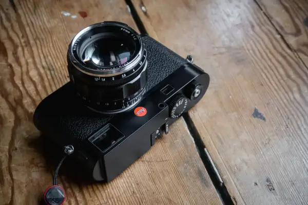 A black Leica M262 camera with a Nokton 50mm f/1.2 lens sits on a wooden surface.