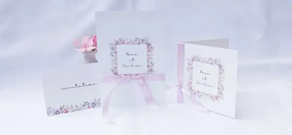 Trois faire-part de mariage délicats, ornés de fleurs pastel et de rubans roses. L'un d'eux mentionne "Rosa et Emilien".