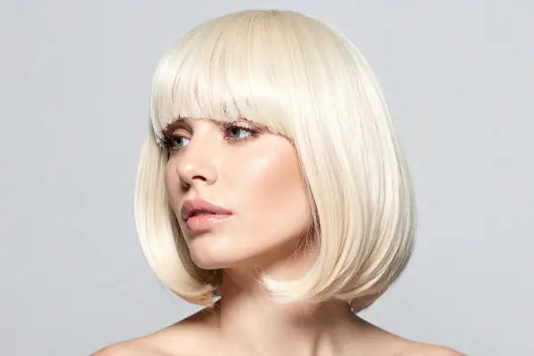 Blond cieniowany bob fryzura z grzywką. Kobieta z delikatnym makijażem patrzy w bok.