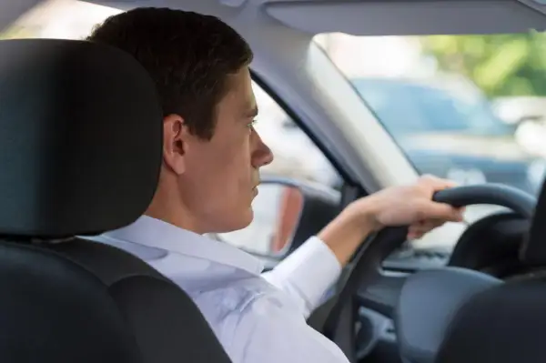 Uomo al volante, con la mano sul volante. Si può guidare una macchina intestata ad un familiare, anche se non è la sua.