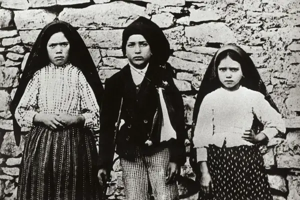Trójka dzieci, w tym siostra Łucja z Fatimy, pozuje przed kamiennym murem.
