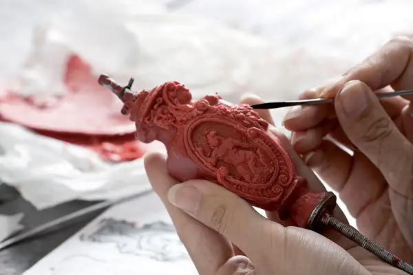 Mani esperte rifiniscono un oggetto in cera rossa, un'opera d'arte che ricorda la **fondazione Cologni**. Dettagli intricati prendono forma sotto gli strumenti.