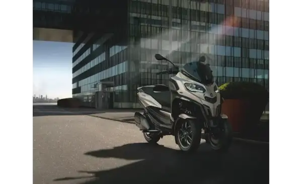 Nowoczesny Piaggio MP3, czy wersja 400 czy 500, parkuje przed szklanym budynkiem.