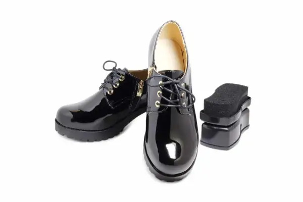 Paire de chaussures vernies synthétiques noires avec un applicateur de cirage. Parfait pour l'entretien des chaussures vernies synthétiques.