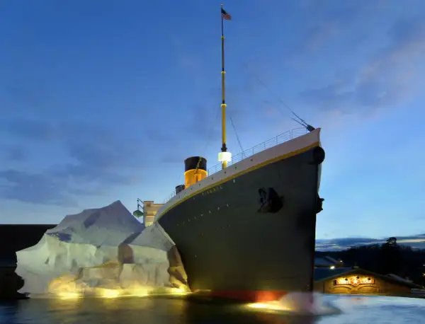 A replica of the Titanic ship is shown at dusk, with an iceberg and the White Star Line building.