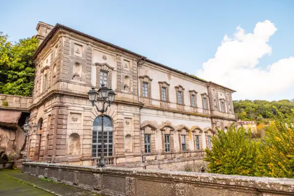 Il **Palazzo Chigi Soriano nel Cimino**, con la sua facciata imponente e le finestre eleganti, si staglia contro un cielo azzurro con nuvole bianche.