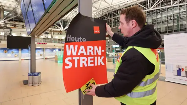 Ein Mann mit Warnweste befestigt ein Schild "Heute WARN-STREIK" an einem Pfosten. Hier wird heute gestreikt.