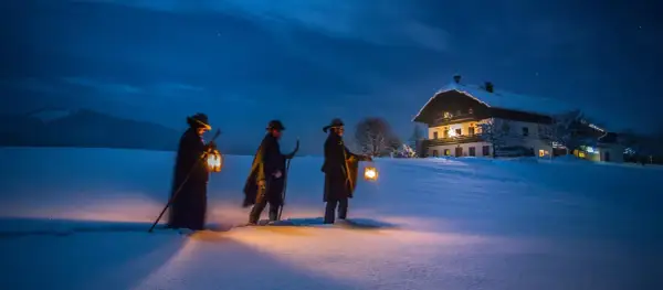 Trzej mężczyźni z latarniami idą przez zaśnieżone pole do domu. Może to scena z czasów, kiedy powstała kolęda "Cicha noc".