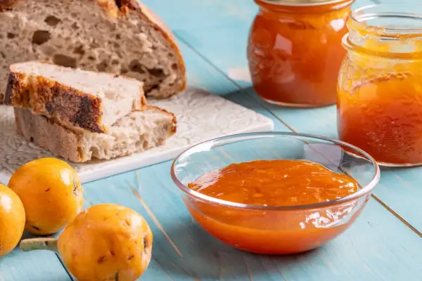 Pane rustico, nespole fresche e una ciotola colma di deliziosa marmellata di nespole, pronta per essere gustata.