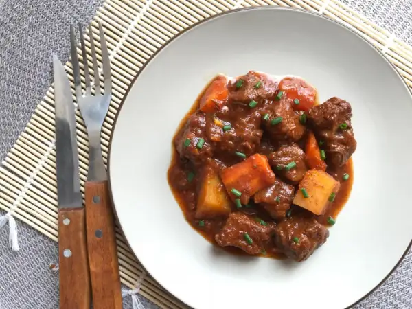 Un plato de goulash de ternera con trozos de patata y zanahoria, adornado con cebollino. Cubiertos de una rica salsa.
