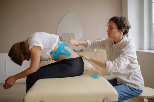 Fizjoterapeutka z taśmami kinezjotaping na plecach pacjentki. Zastanawiasz się, ile zarabia fizjoterapeuta w Norwegii?
