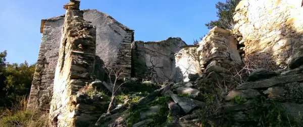 Ruines d'un village abandonné en Haute-Corse, envahies par la végétation. Les murs de pierre s'effondrent sous le ciel bleu.