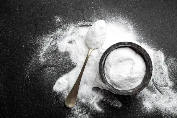 Un cucchiaio e una ciotola pieni di carbonato di sodio, mostrando i suoi molteplici usi in cucina e per la pulizia.