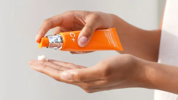 Mani che dosano una crema con vitamina C sulla pelle, per un trattamento illuminante e antiossidante.