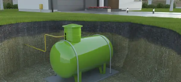 Podziemny zbiornik na gaz, prawdopodobnie izobutan, w zielonym kolorze, podłączony żółtą rurą do domu.