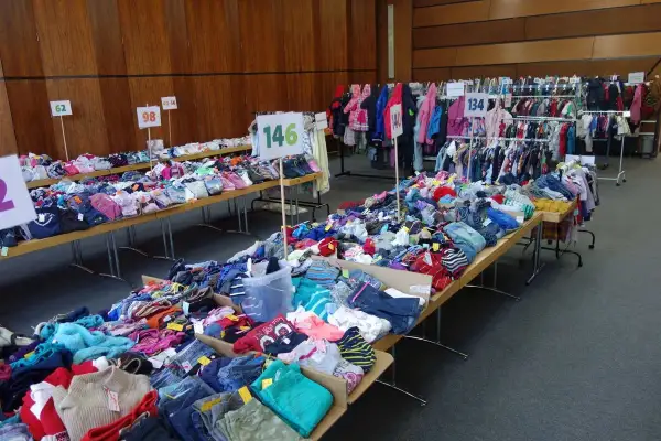 Großer kinderflohmarkt in Bergisch Gladbach mit Kleidung auf Tischen und Kleiderstangen.