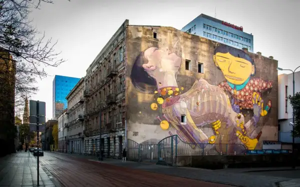 Imponujące street art na ścianie kamienicy, przedstawiające surrealistyczną scenę z postaciami i elementami anatomicznymi.