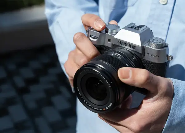 Dłonie trzymające srebrny aparat Fujifilm X-T50 z obiektywem Fujinon.