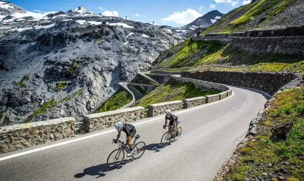 Dwóch kolarzy pokonuje serpentyny na przełęczy Stelvio, otoczeni surowym, górskim krajobrazem.