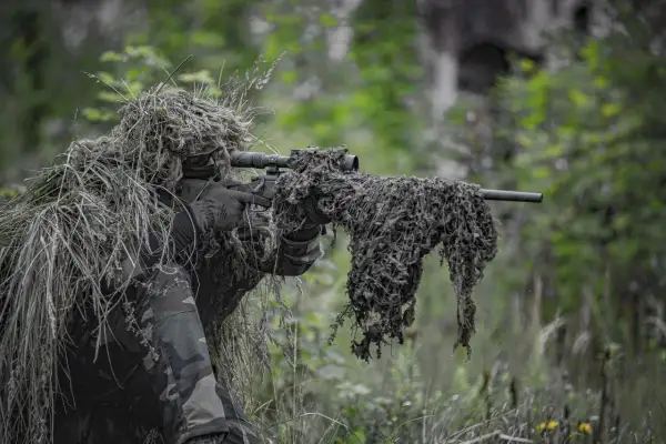 Un francotirador camuflado en un bosque, listo para la acción. El airsoft, un deporte que simula combates, requiere sigilo y estrategia.