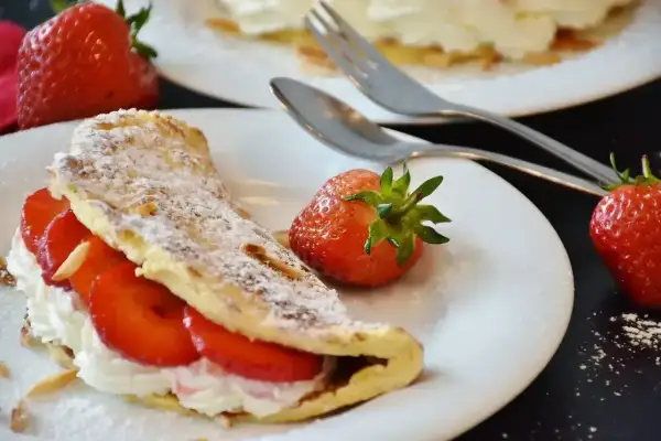 Pyszny omlet z białek z bitą śmietaną i truskawkami, posypany cukrem pudrem i płatkami migdałów.