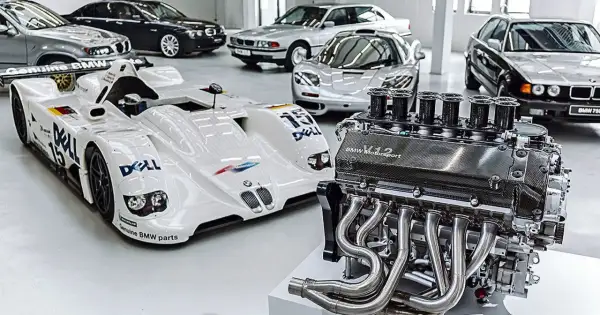 Silnik V12 BMW Motorsport obok białego bolidu wyścigowego i kilku klasycznych BMW.