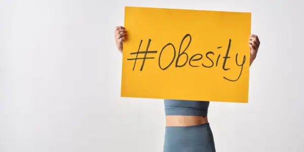 Osoba trzymająca tabliczkę z napisem #Obesity. Problem otyłości w Polsce staje się coraz poważniejszy.
