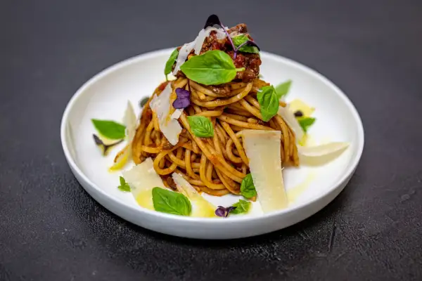 Pyszne spaghetti alla norma z sosem pomidorowym, bakłażanem, bazylią i parmezanem, podane na białym talerzu.